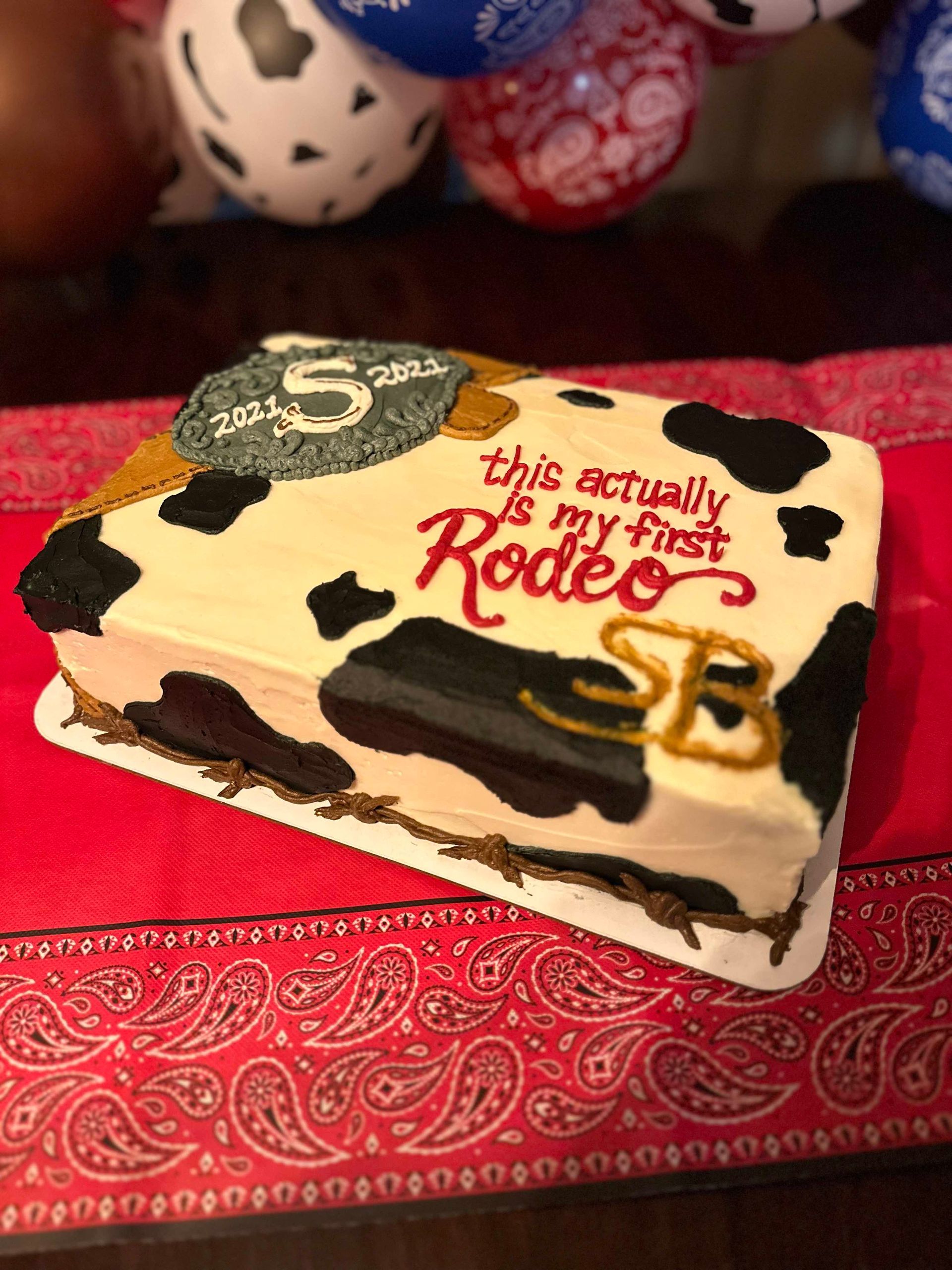 A rectangular cake decorated with black and white cow print, gold rope, and