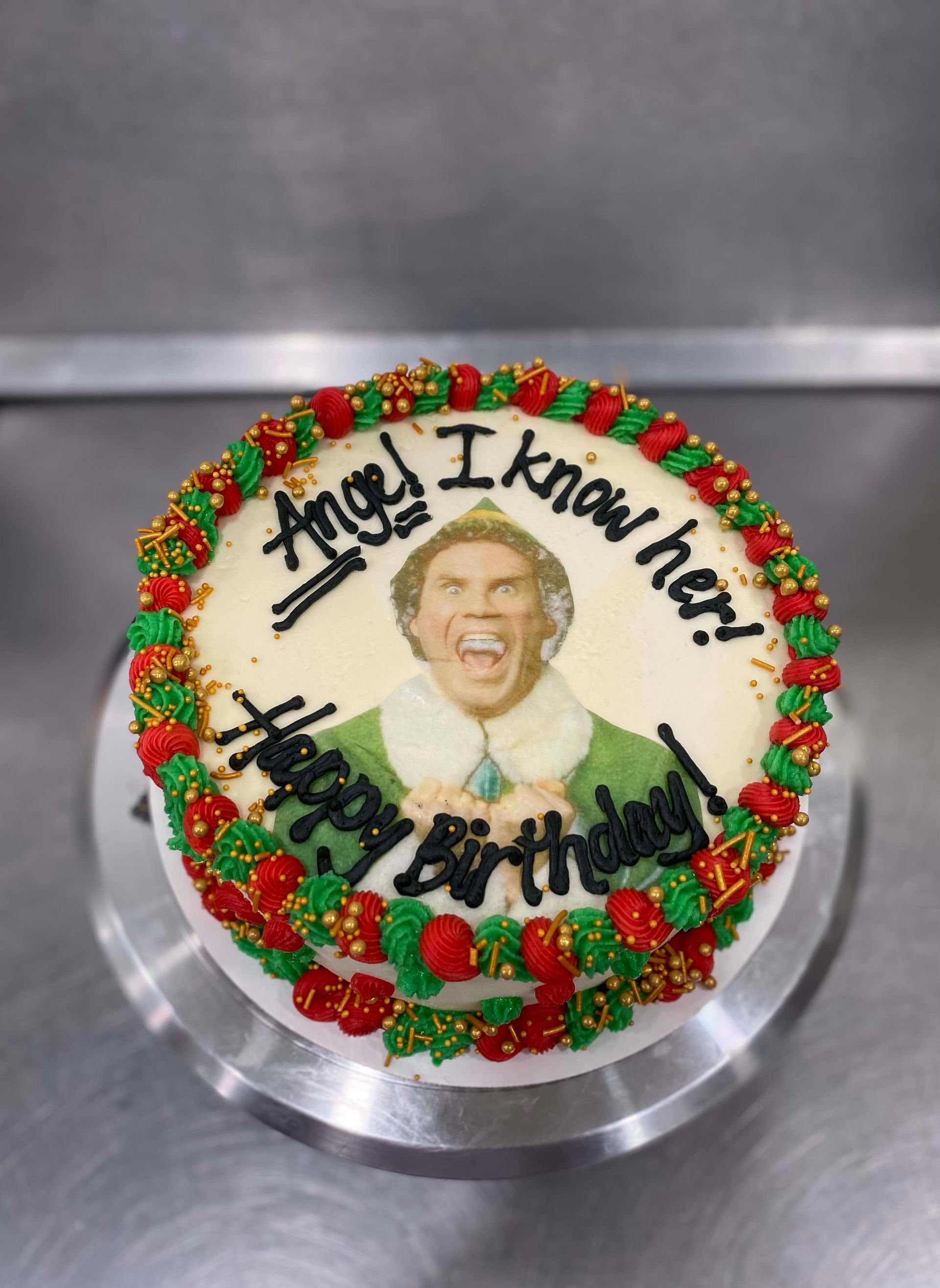 A round cake decorated with a scene from the movie Elf, reading