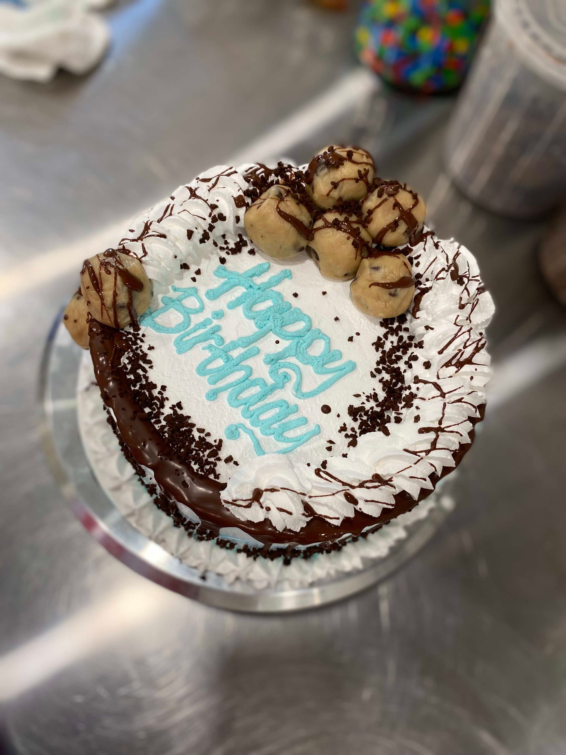 A chocolate birthday cake topped with white frosting, light-colored cookie dough balls, and
