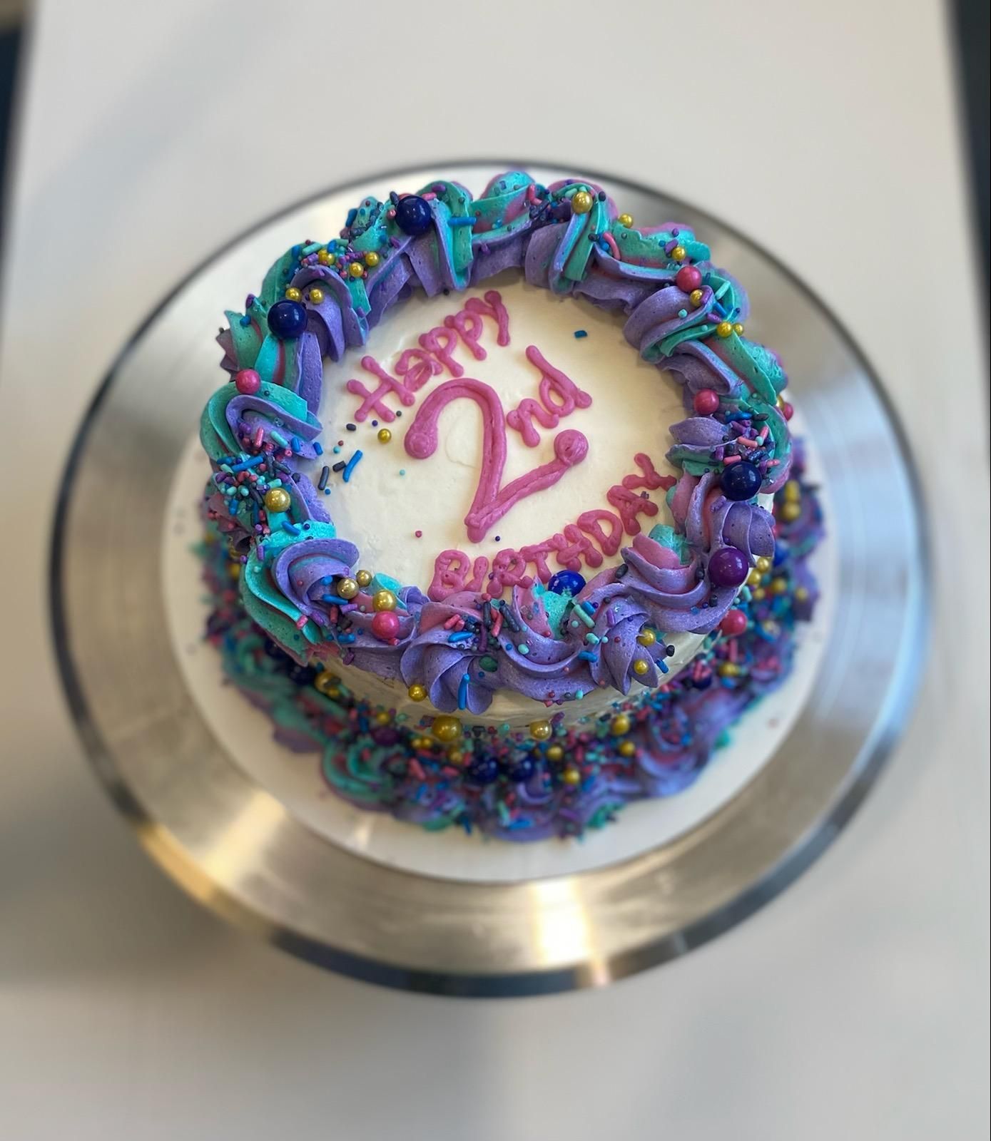 A round cake on a metal stand with pink 