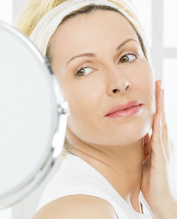 a woman is looking at her face in a mirror a woman is looking at her face in a mirror