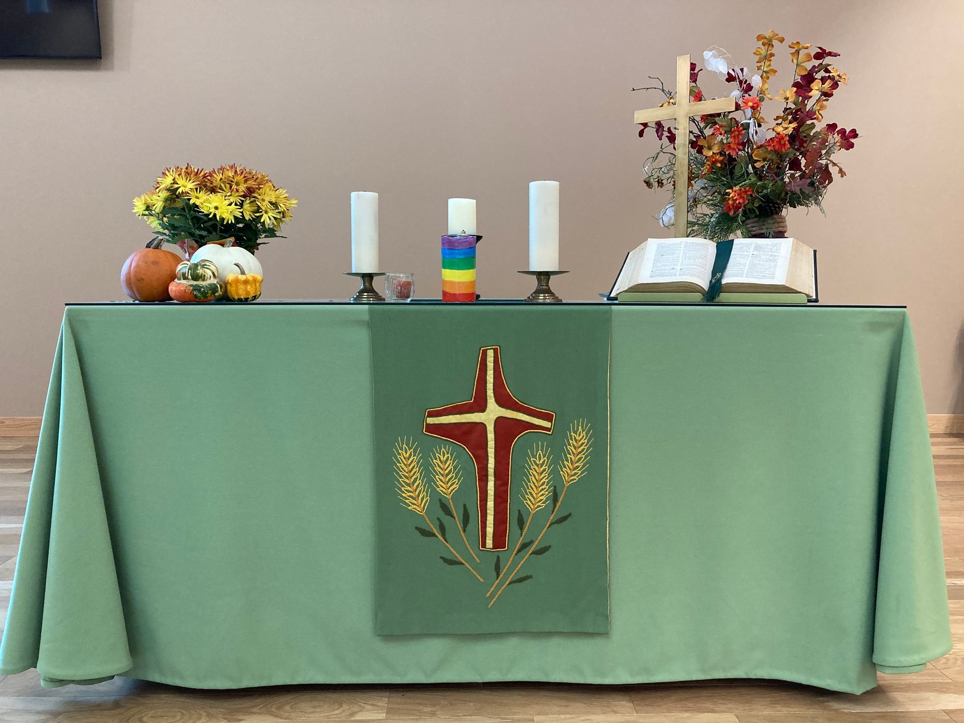 Altar table with green tablecloth, candles, autumnal decorations, and an open bible. 