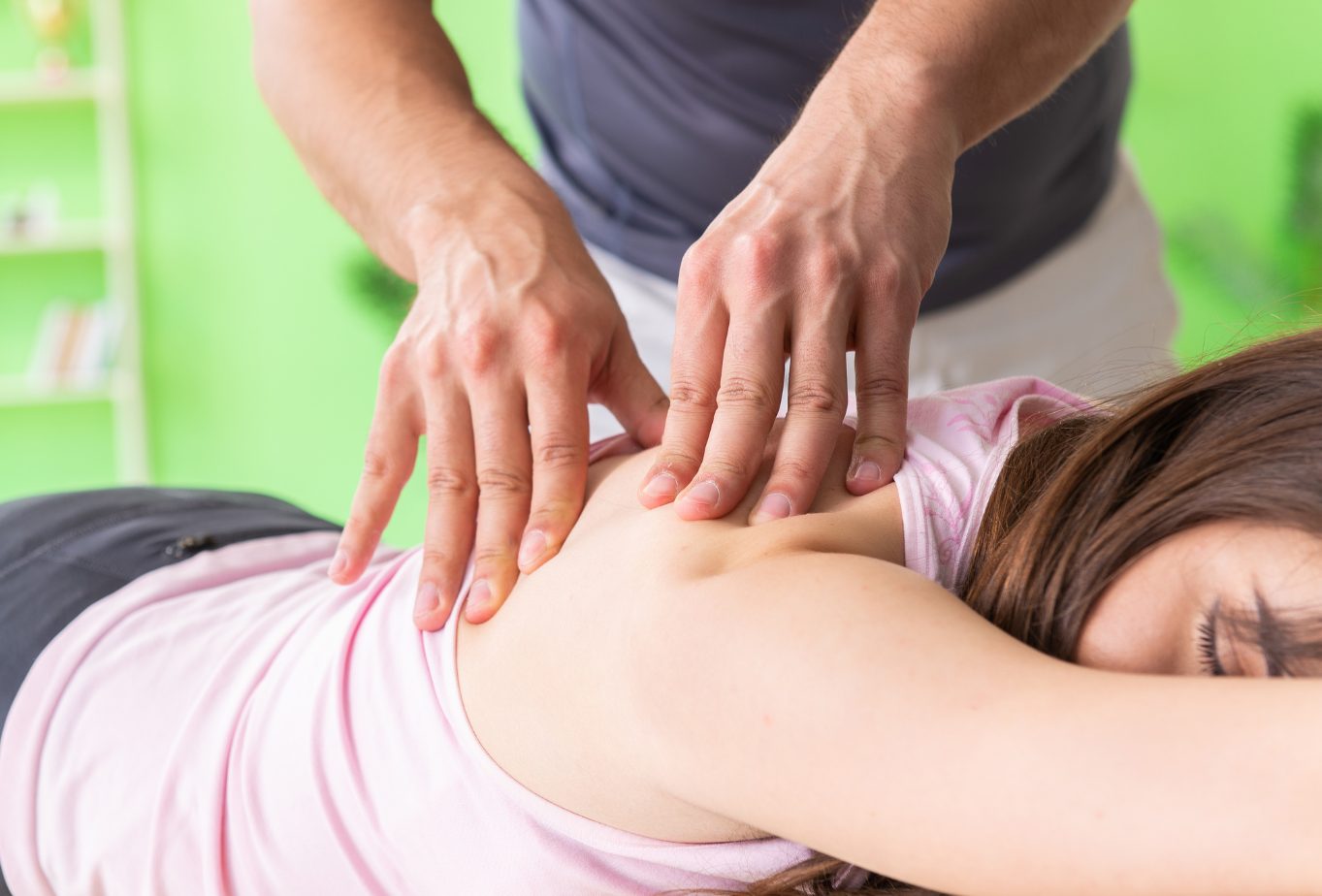 Massage therapist pressing a woman's back and shoulders while she lies face down on a table