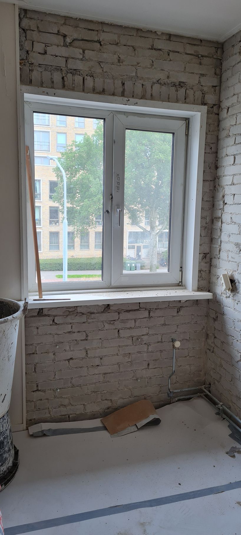 Een binnenruimte van onbewerkt baksteen met een wit kozijn en een onafgewerkte vloer, waaruit renovatiewerkzaamheden blijken.