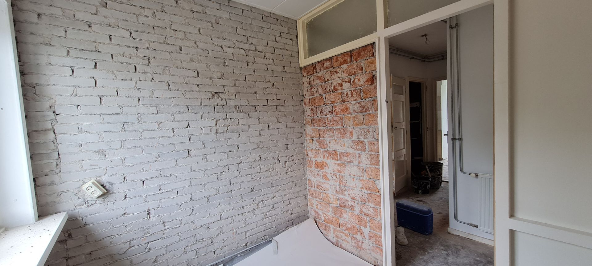 Kale kamer in renovatie met zichtbare bakstenen muren en een deuropening omlijst met witte kozijnen.