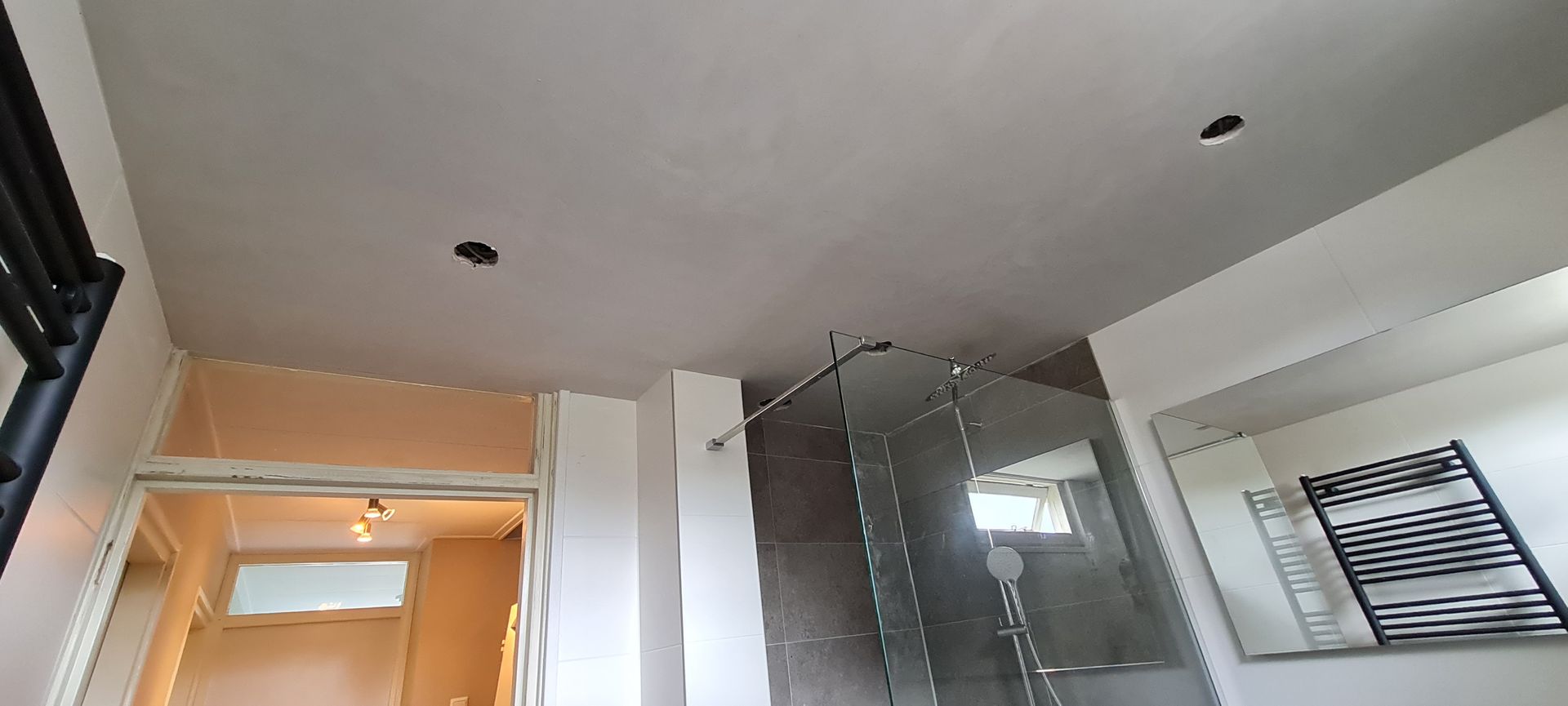 Moderne badkamer met glazen douchecabine, wit plafond en handdoekrek aan de muur.