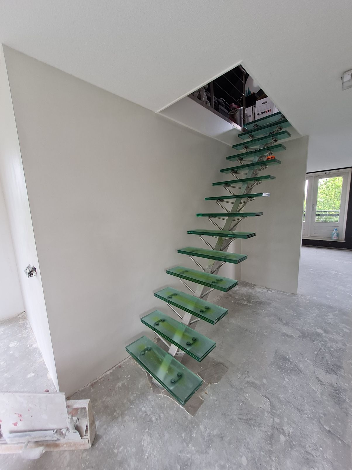 Gedeeltelijk gebouwde trap met groene treden in een onafgewerkte binnenkamer.