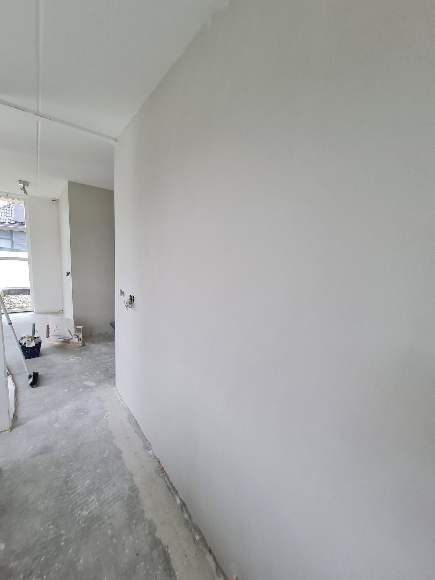 Onafgewerkte witte gang met kale vloer en bouwmaterialen aan de linkerkant.