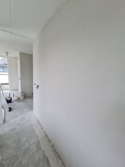Onafgewerkte witte gang met kale vloer en bouwmaterialen aan de linkerkant.