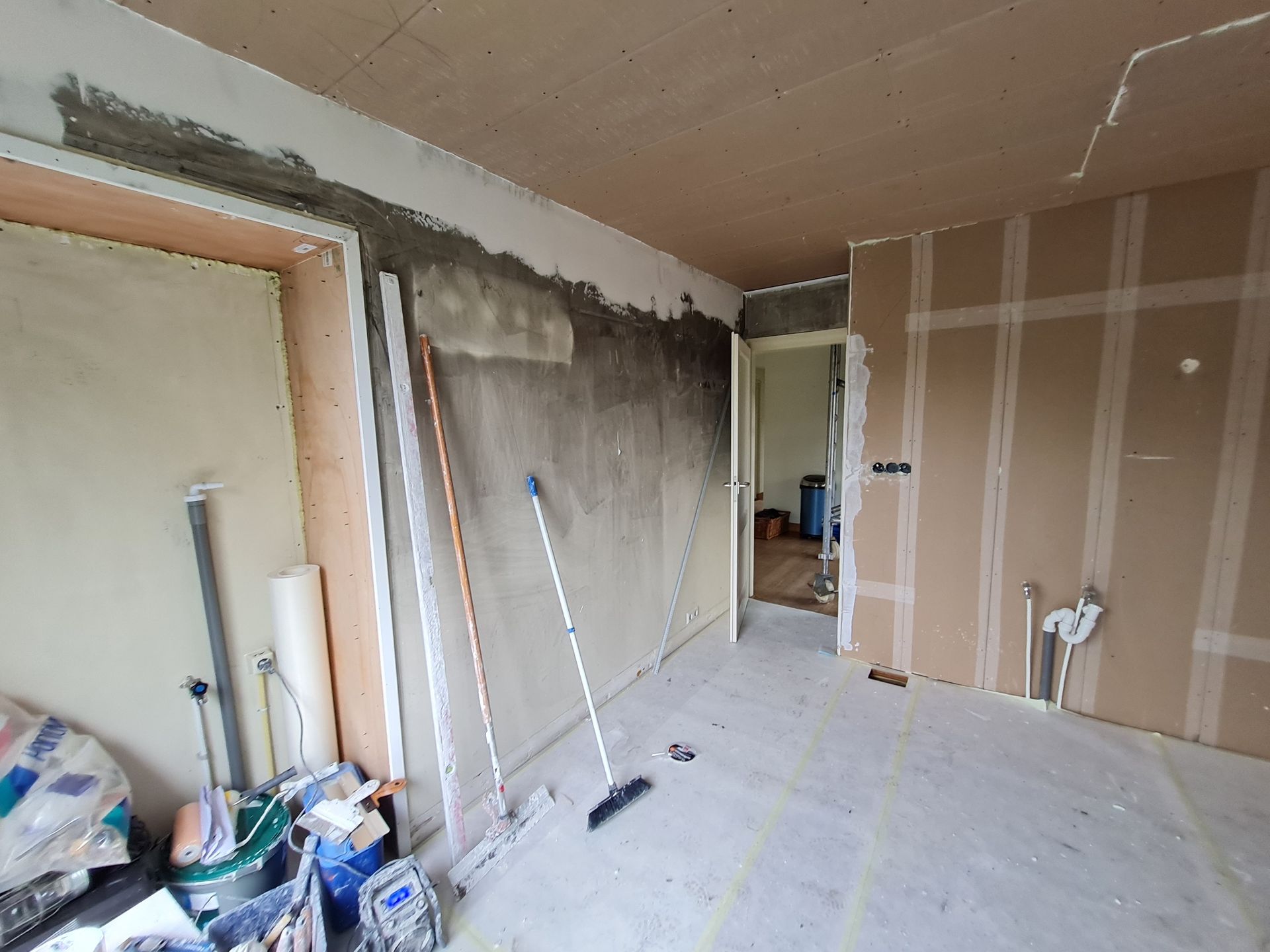 Gedeeltelijk gerenoveerde kamer met gipsplaten, gereedschap en puin op de vloer.