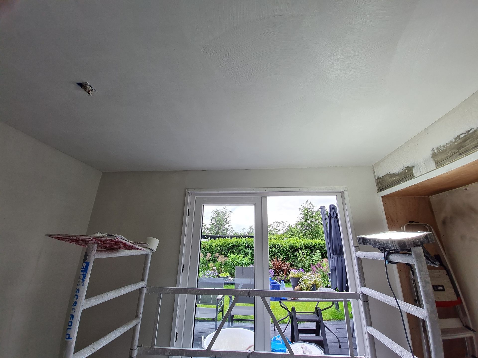 Lichte kamer met openslaande balkondeuren, droogrekken en terrasmeubilair dat buiten zichtbaar is.