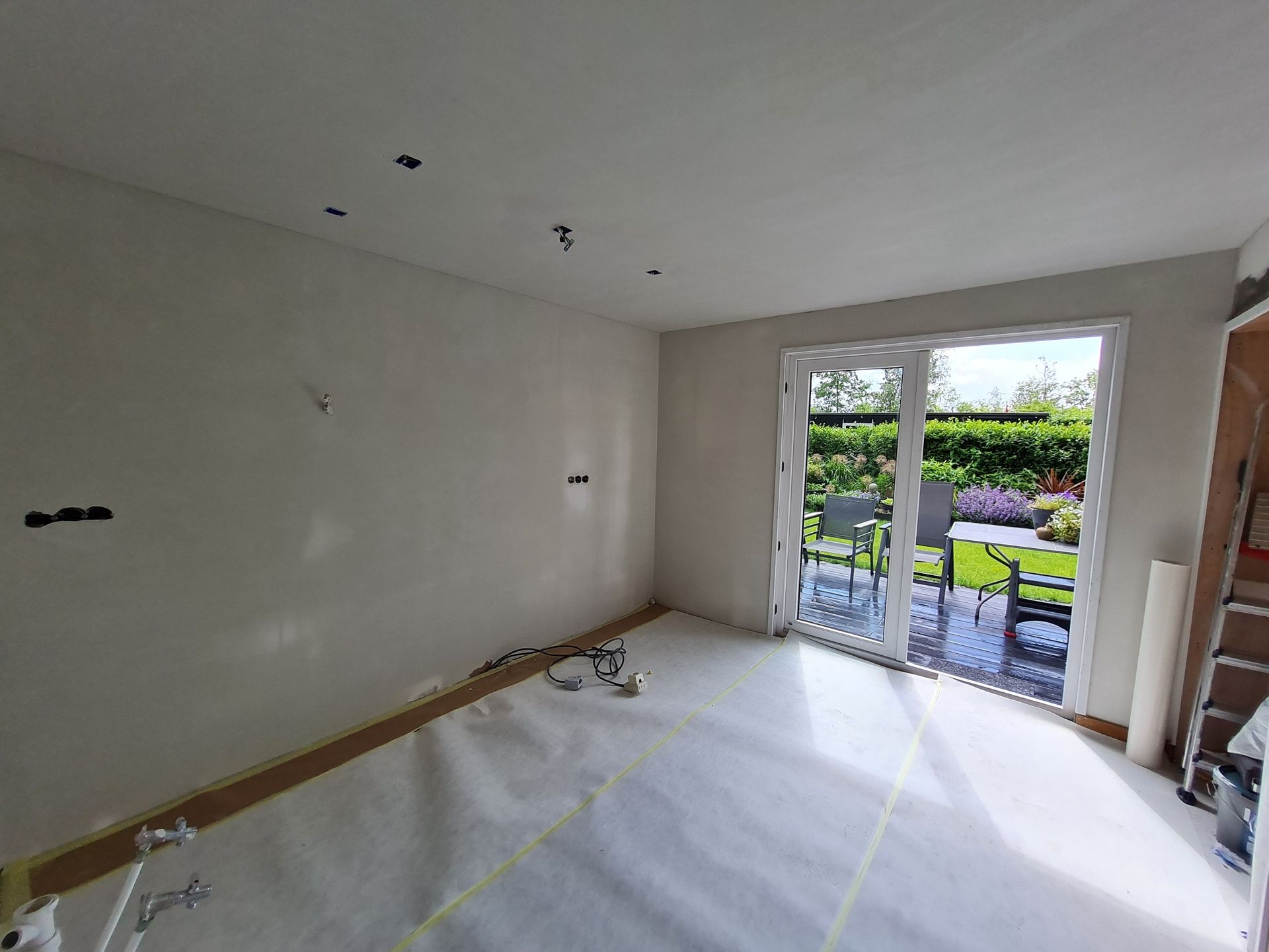 Lege, ongemeubileerde kamer met witte muren, openslaande deuren naar het terras en zonlicht op de vloer.