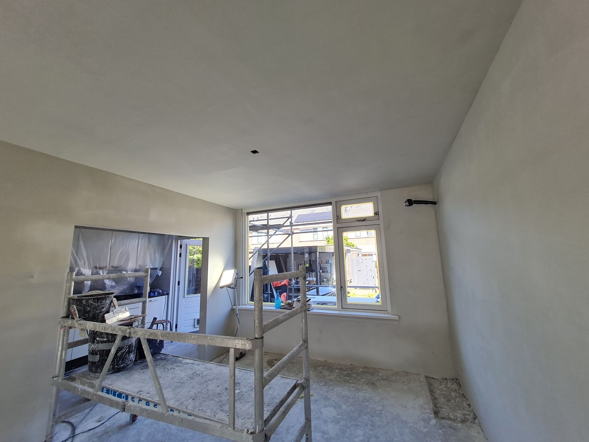 Renovatieruimte met gestucte muren, raam en steigers aan de binnenkant.