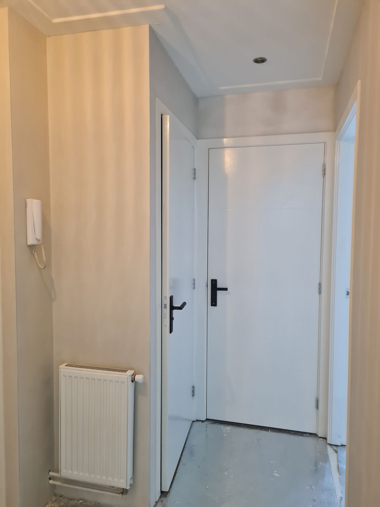 Smalle gang met beige gestreepte muren, witte deuren en een radiator aan de linkerkant.