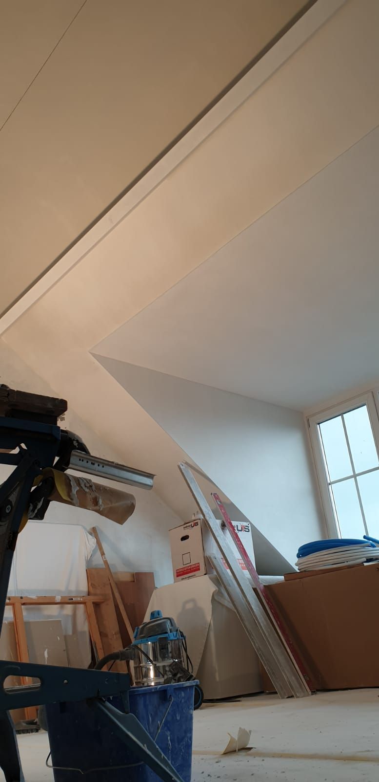 Zolderinterieur met schuin plafond, ladder, dozen en een dakraam.