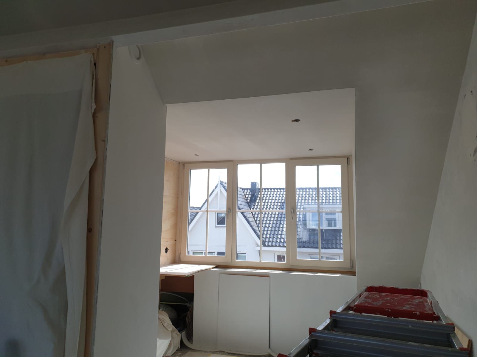 Gerenoveerde kamer met een groot raam, witte muren en een kast onder de vensterbank.