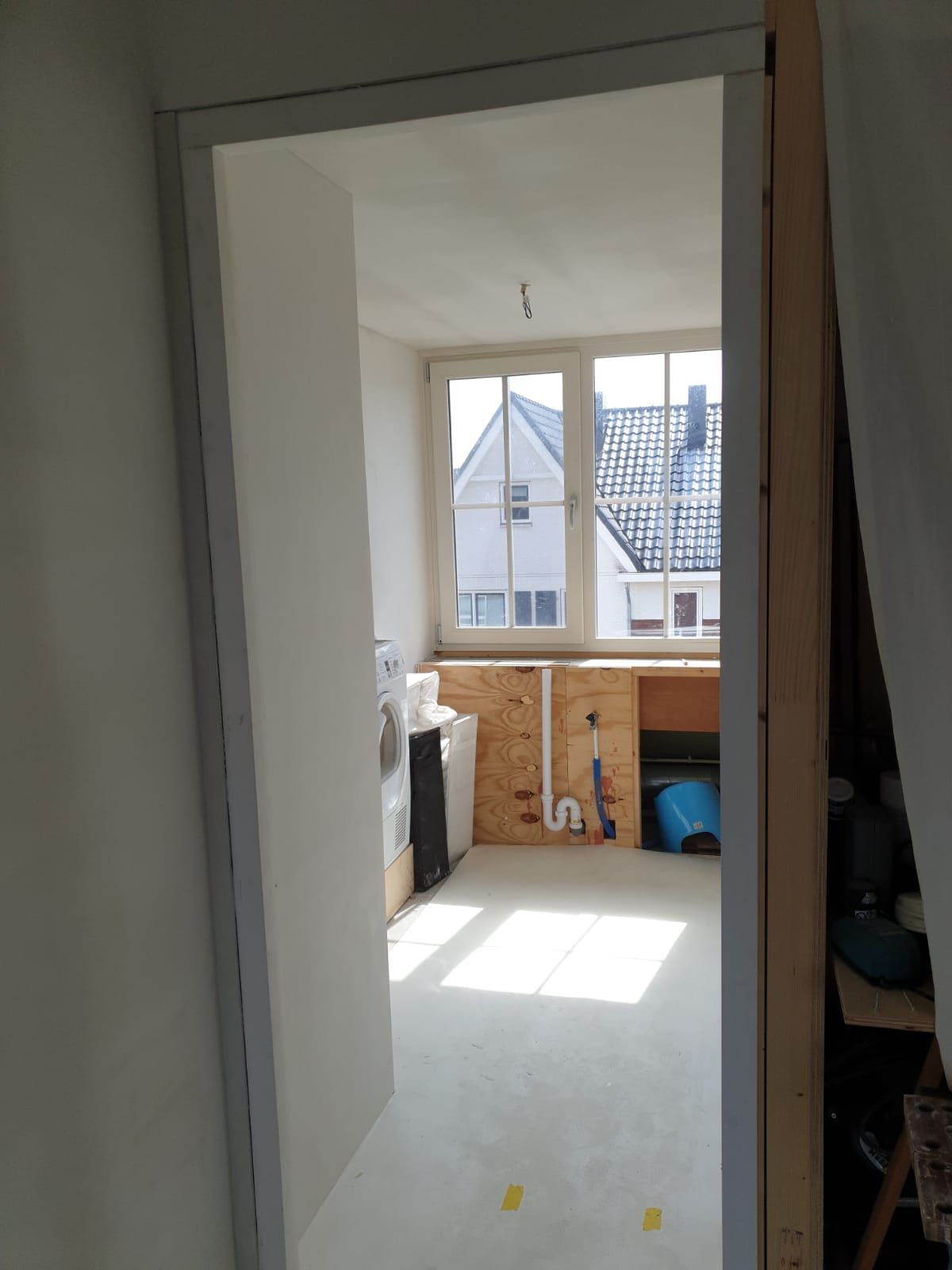 Een open deuropening leidt naar een lichte kamer met een raam en een gedeeltelijk afgewerkt interieur.