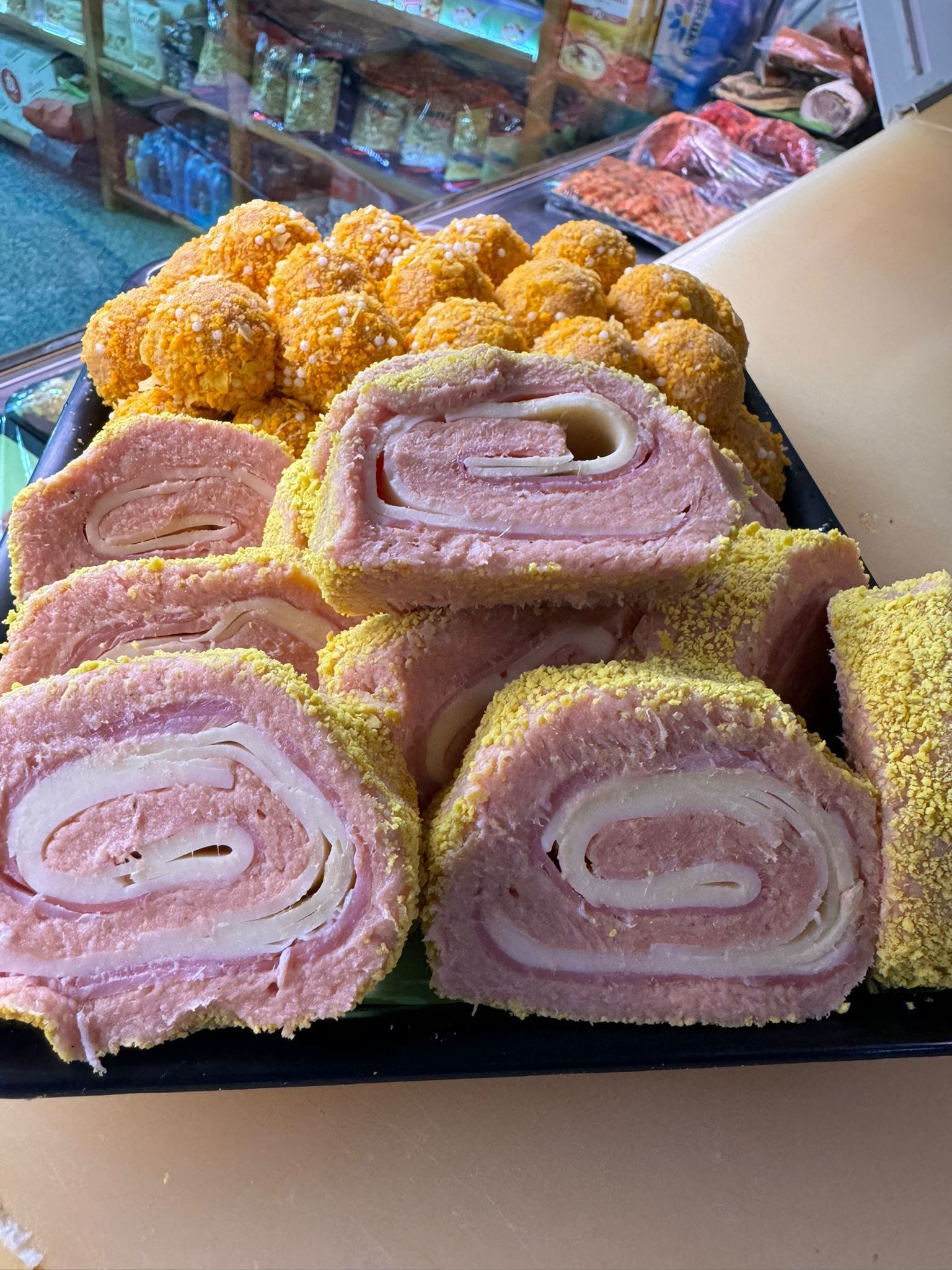 Involtini di prosciutto e formaggio e palline impanate gialle, disposti su un vassoio in un banco gastronomia.