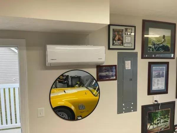 Wall with air conditioner, round mirror reflecting a yellow car, and framed pictures and car memorabilia