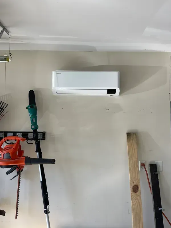Wall-mounted white air conditioner above tools hanging on a garage wall