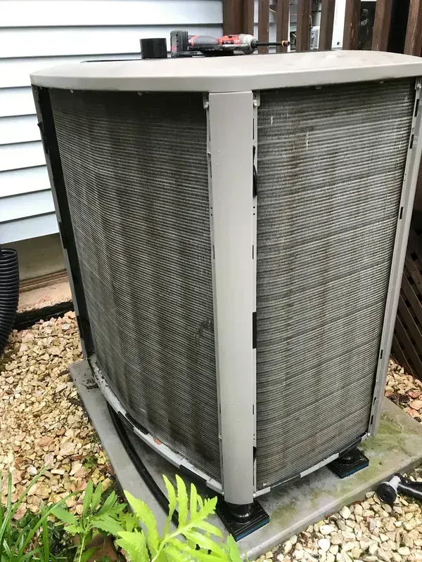 Outdoor HVAC condenser unit beside a house, with gray metal panels and a beige top cover.