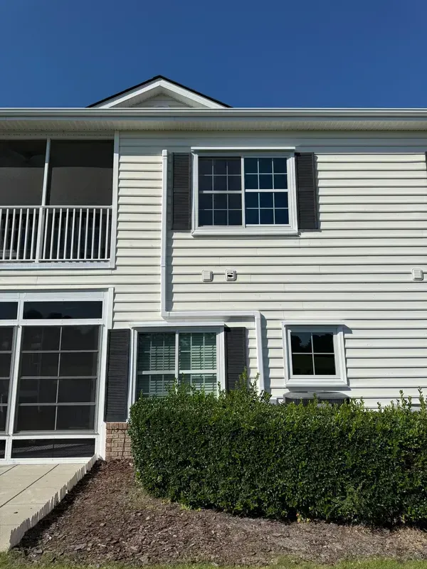 Two-story beige townhouse with white trim, screened porch, and a small front hedge under a blue sky