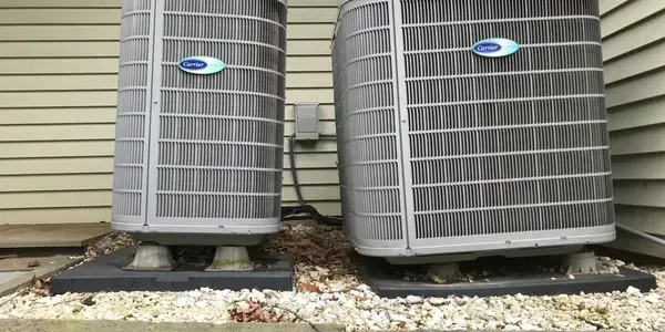 Two outdoor HVAC condenser units beside a house on gravel pads.