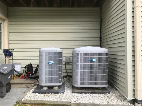 Two gray outdoor air conditioning units beside a house under a covered patio.