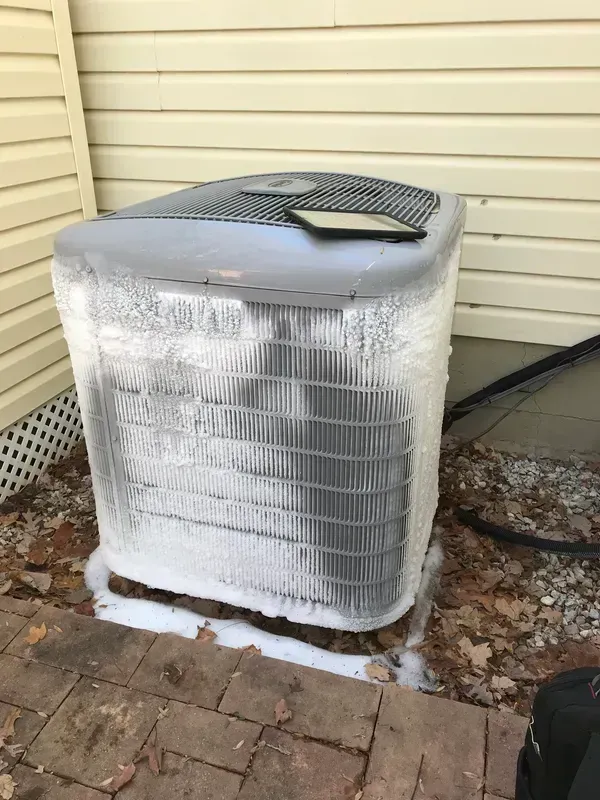 Wrapped outdoor HVAC unit beside beige siding with a vent cover on top and fallen leaves nearby