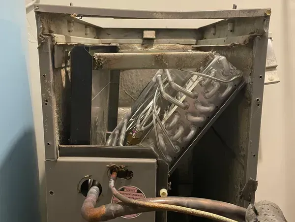 Damaged HVAC unit with bent metal panel and exposed internal wiring inside a wall opening
