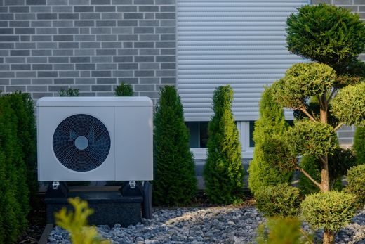 Outdoor HVAC unit beside a brick house wall, with trimmed shrubs and gravel landscaping