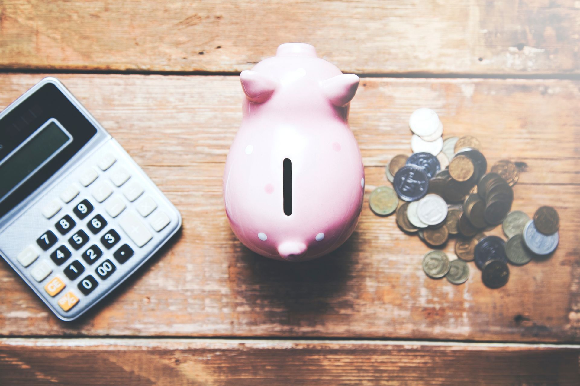 A pink piggy bank with a calculator and coins on a wooden table.