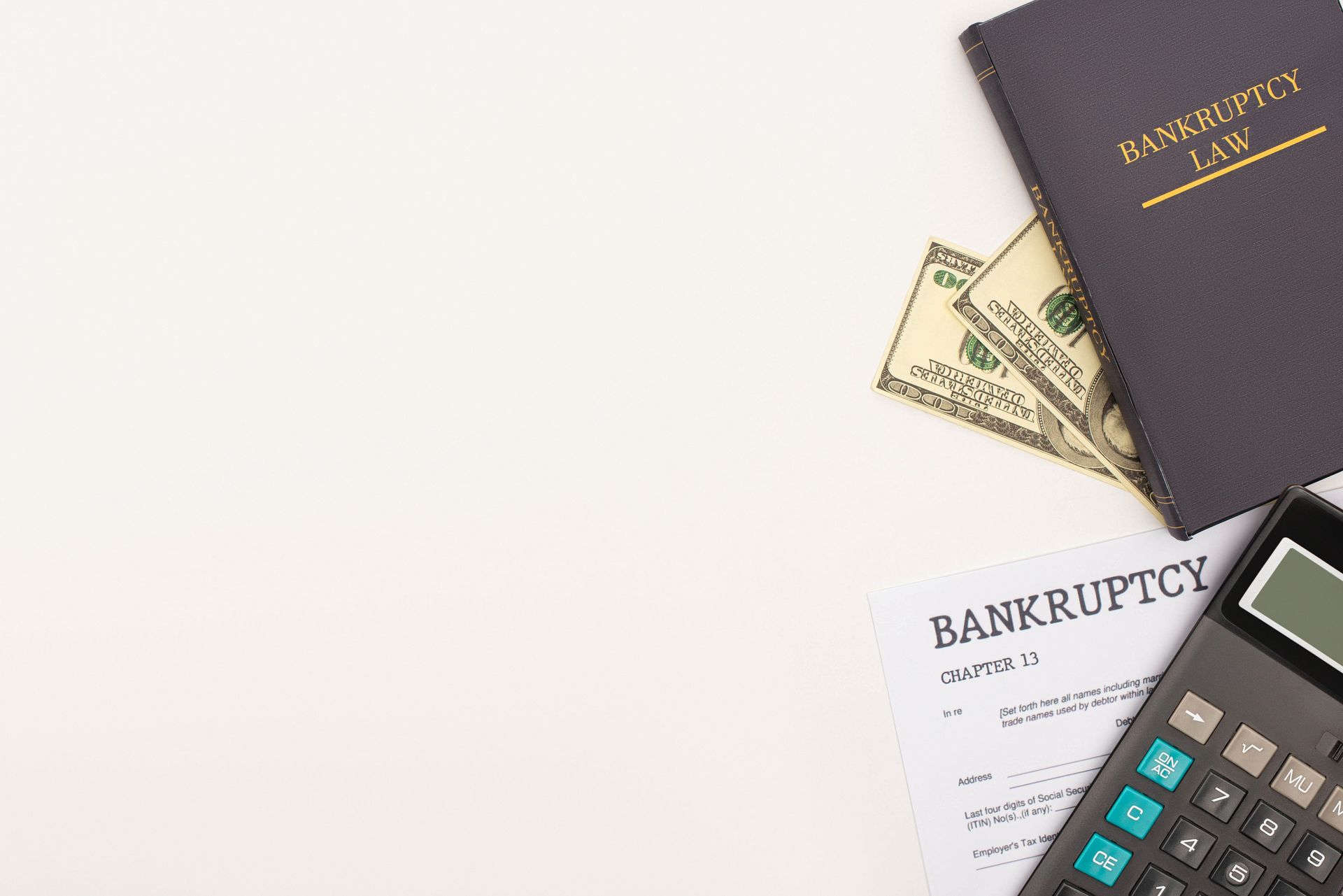 Calculator, bankruptcy form, money, and a black checkbook on a white desk.