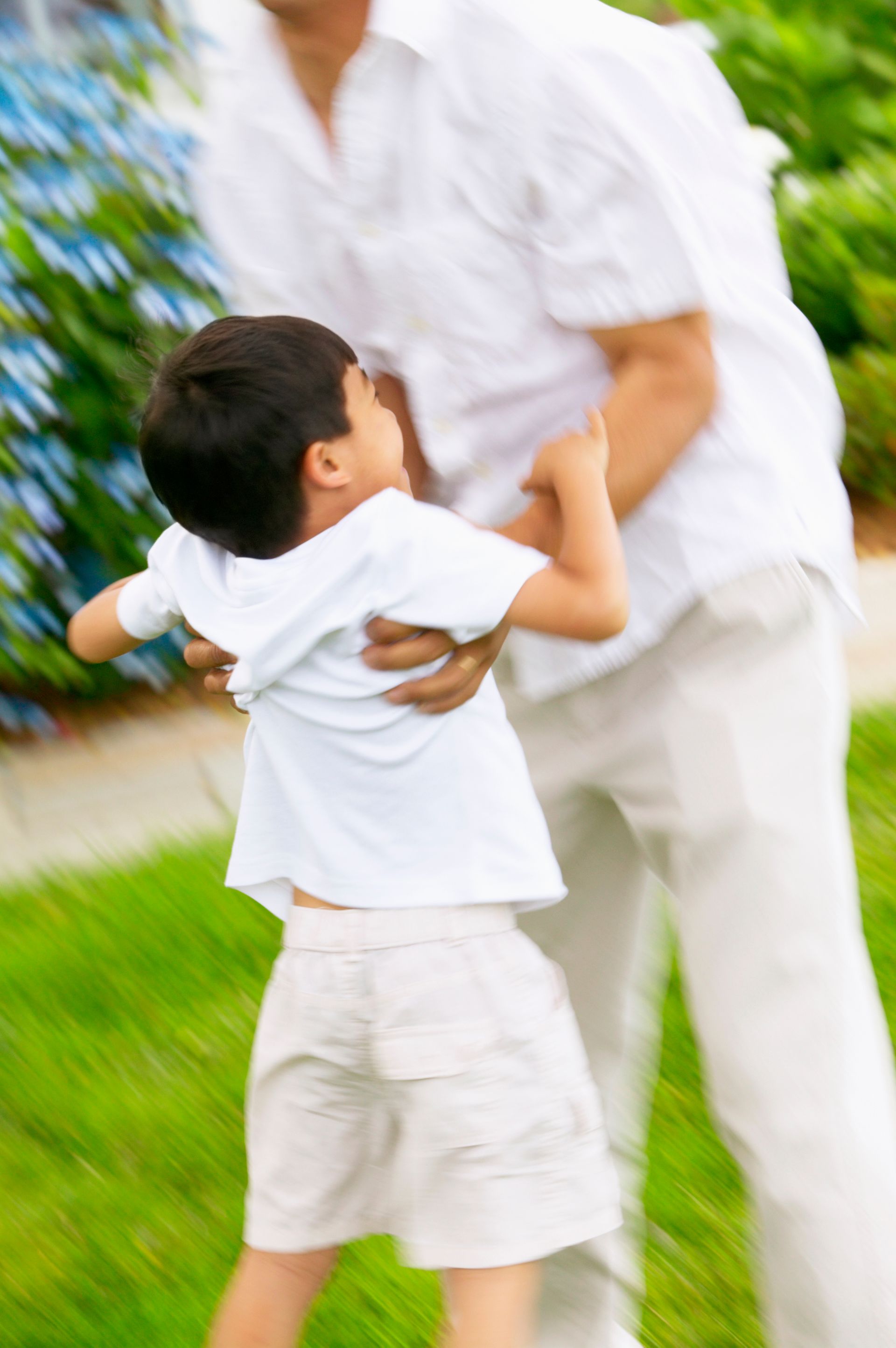 Child being held by an adult in a grassy outdoor setting, blurred motion.