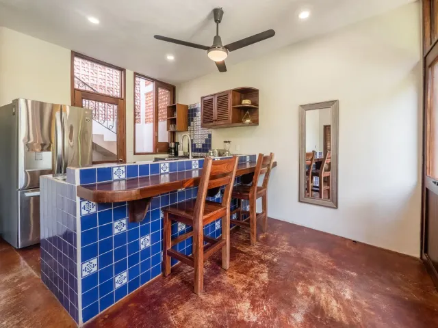Kitchen with blue tile countertop, wooden bar stools, stainless steel fridge, and ceiling fan.