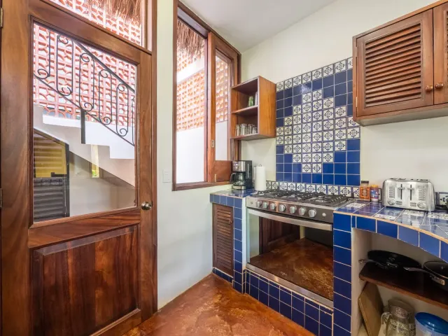 Kitchen with blue tile, wooden cabinets, and a gas stove. Stairs visible through a glass door.