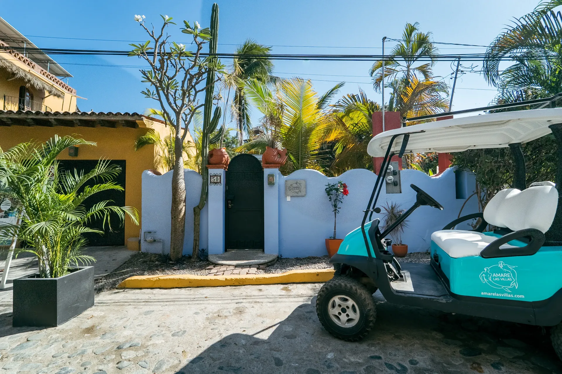 Turquoise golf cart parked outside a blue-walled building with a black door. Yellow building to the left.