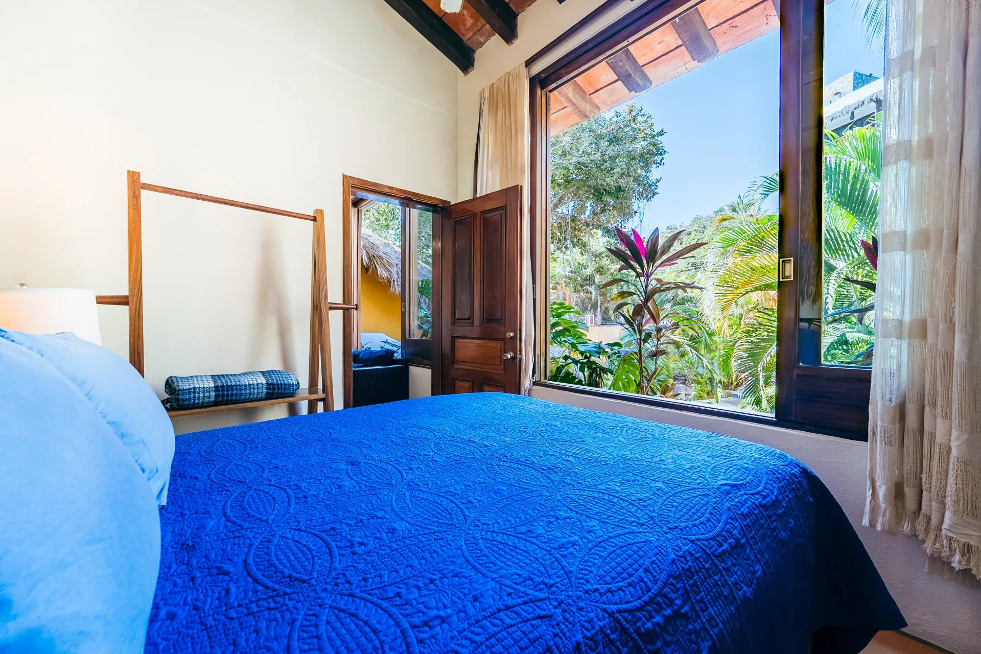 Bedroom with blue bedspread, wooden closet, and a window overlooking a lush garden.