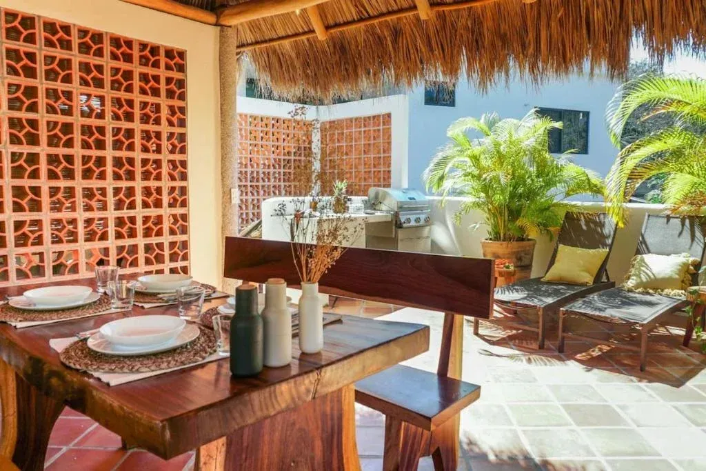 Outdoor dining area with wooden table set for meal, featuring open brickwork and thatched roof.