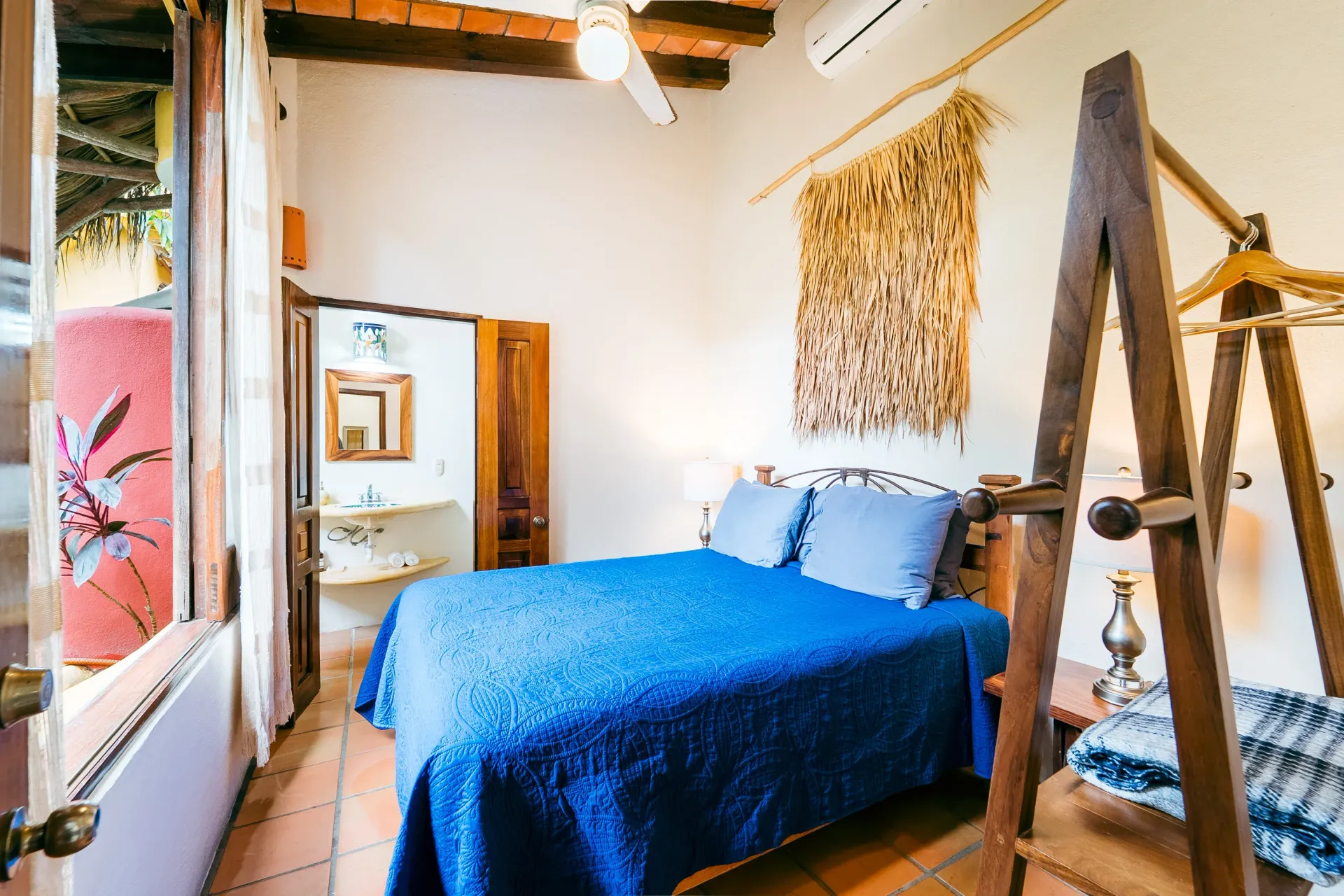 Bedroom with blue bedspread, open doorway to bathroom, decorative wall hanging, rustic style.