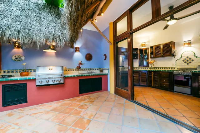 Outdoor kitchen with a grill, red and blue accents, and open doorway to interior.