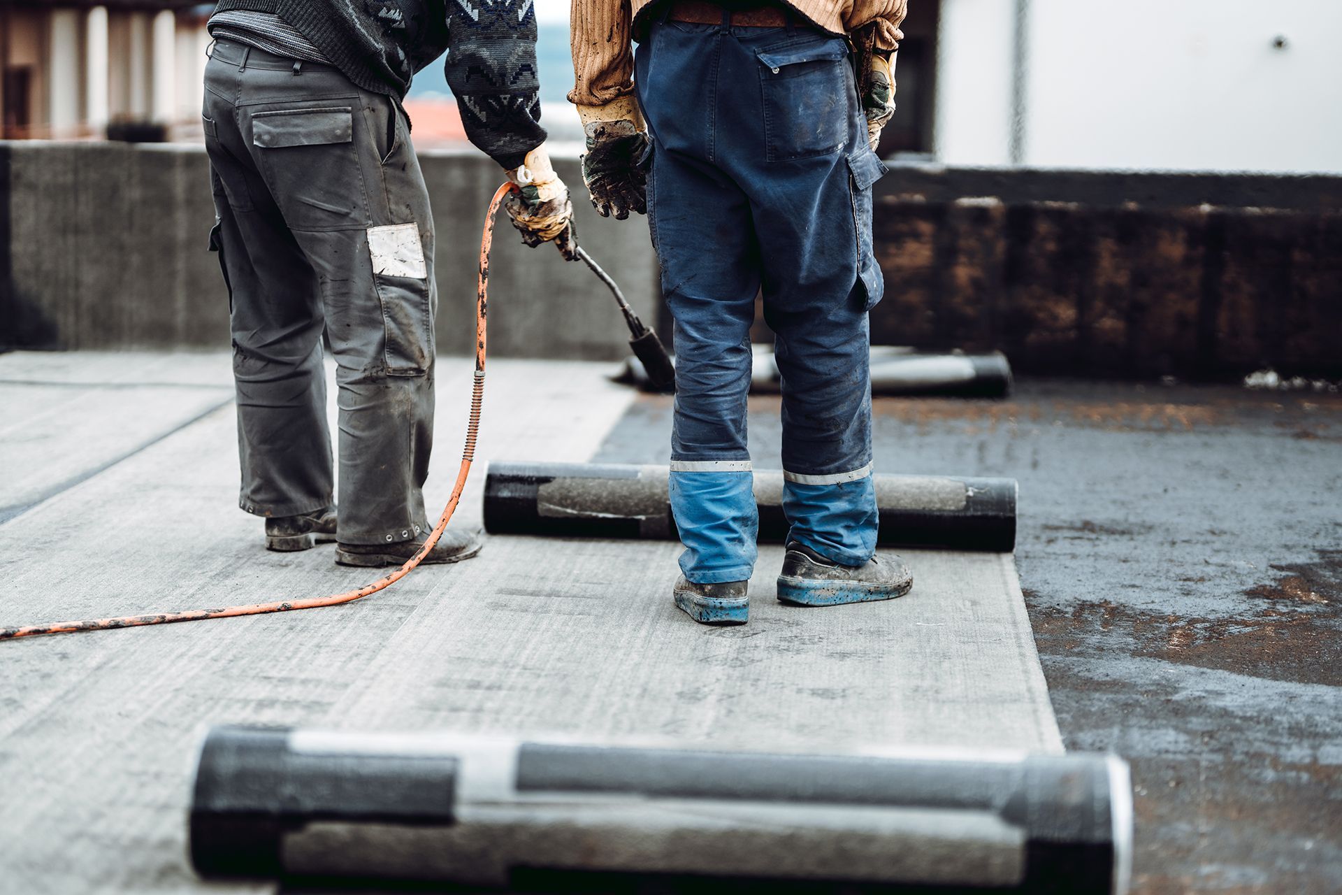 Two men are working on a roof with a torch.