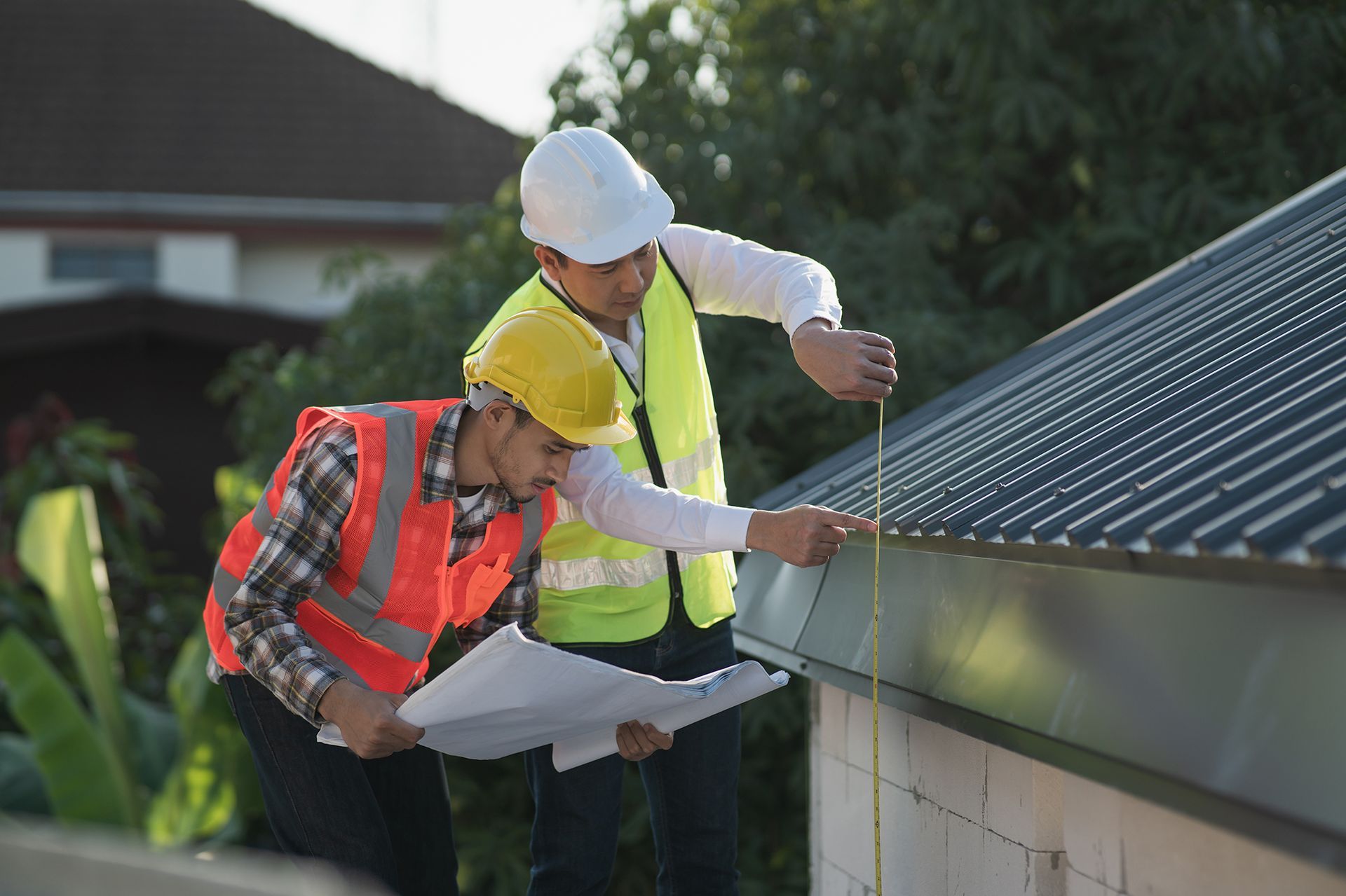 Two construction workers are measuring a roof with a tape measure.