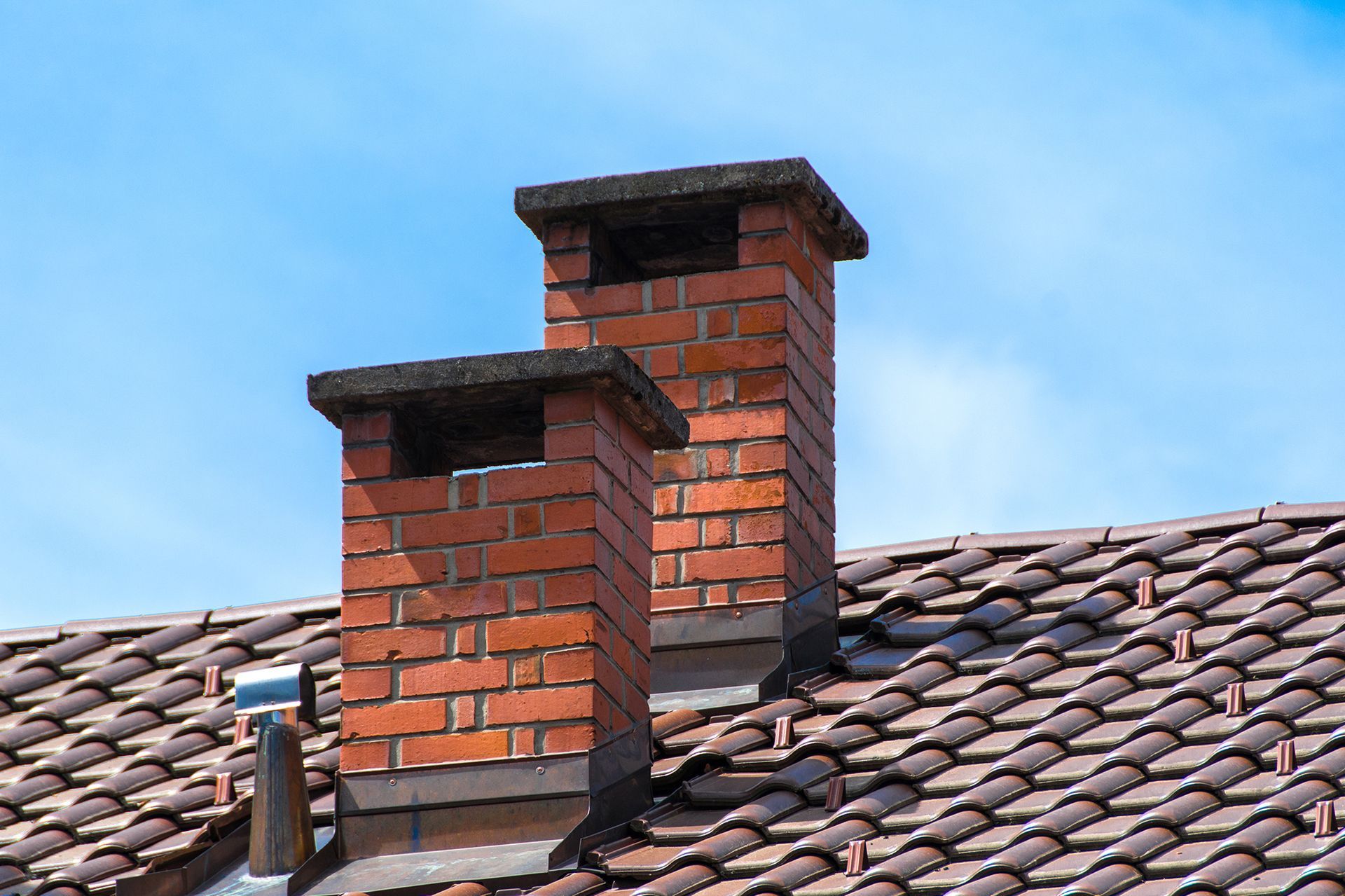 Two brick chimneys on top of a tiled roof.