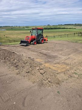 A tractor with a red tiller is tilling dirt on a farm field. Brown and green landscape.