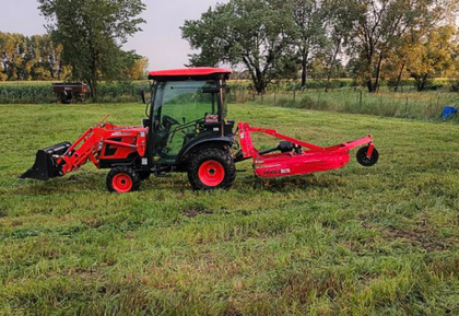 Red tractor with front loader and mower in a grassy field.