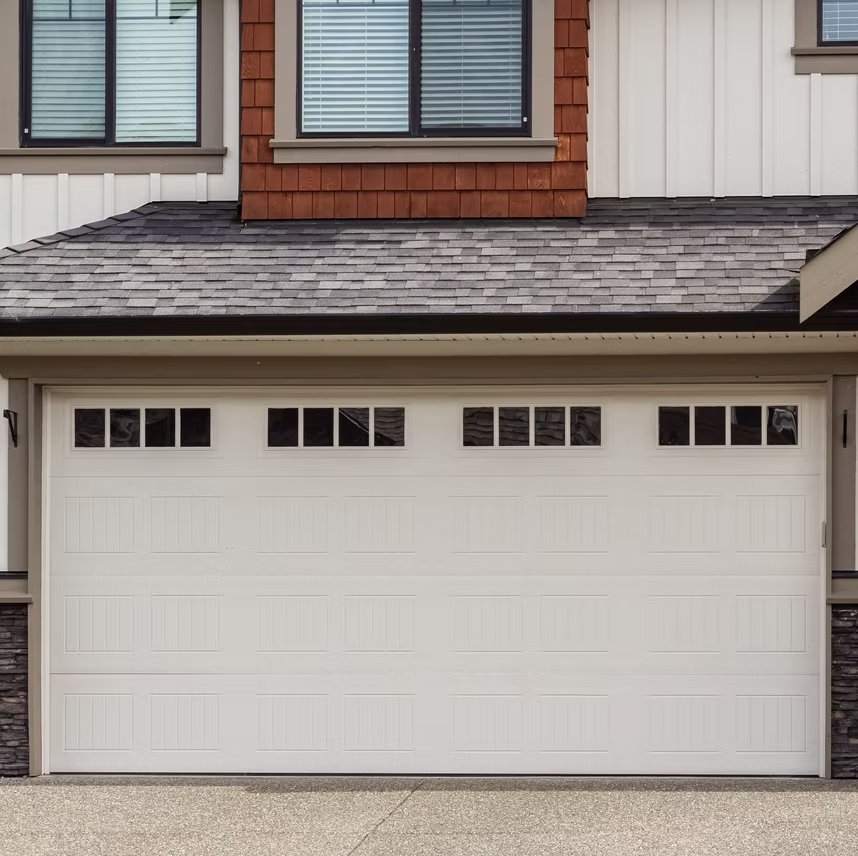 A white garage door with a row of small windows, set below the second story of a modern residential house.