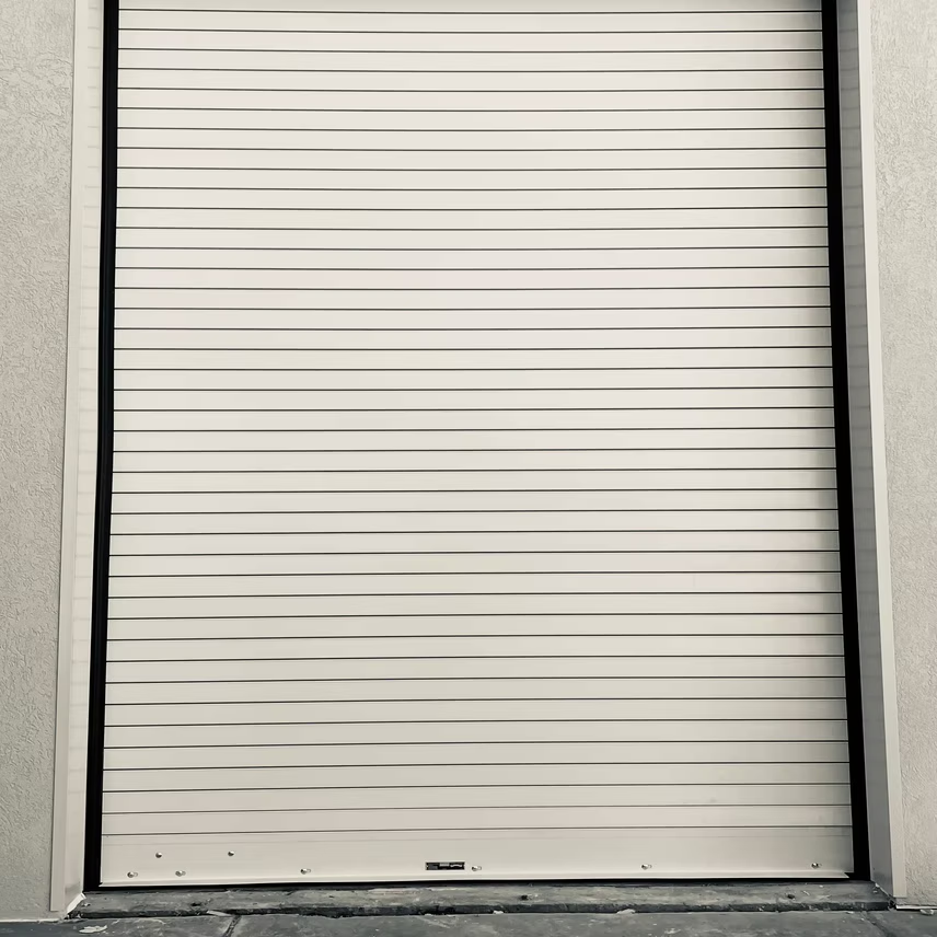 A closed off-white rolling metal security shutter door set within a light-colored building wall.