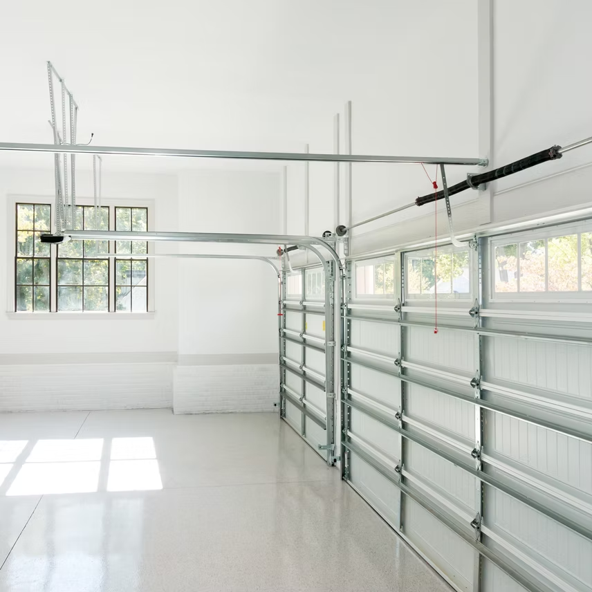 A clean, white garage interior showing a sectional garage door, metal tracks, and a window on the far wall.