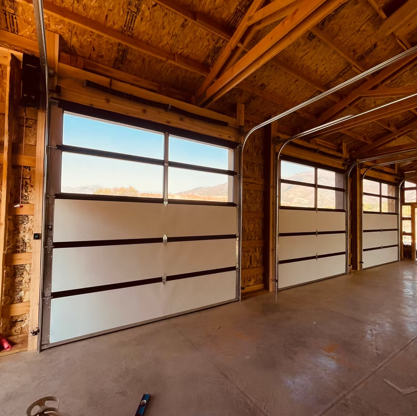 Three garage doors with top glass panels and white lower sections installed in a wooden garage with an unfinished interior.